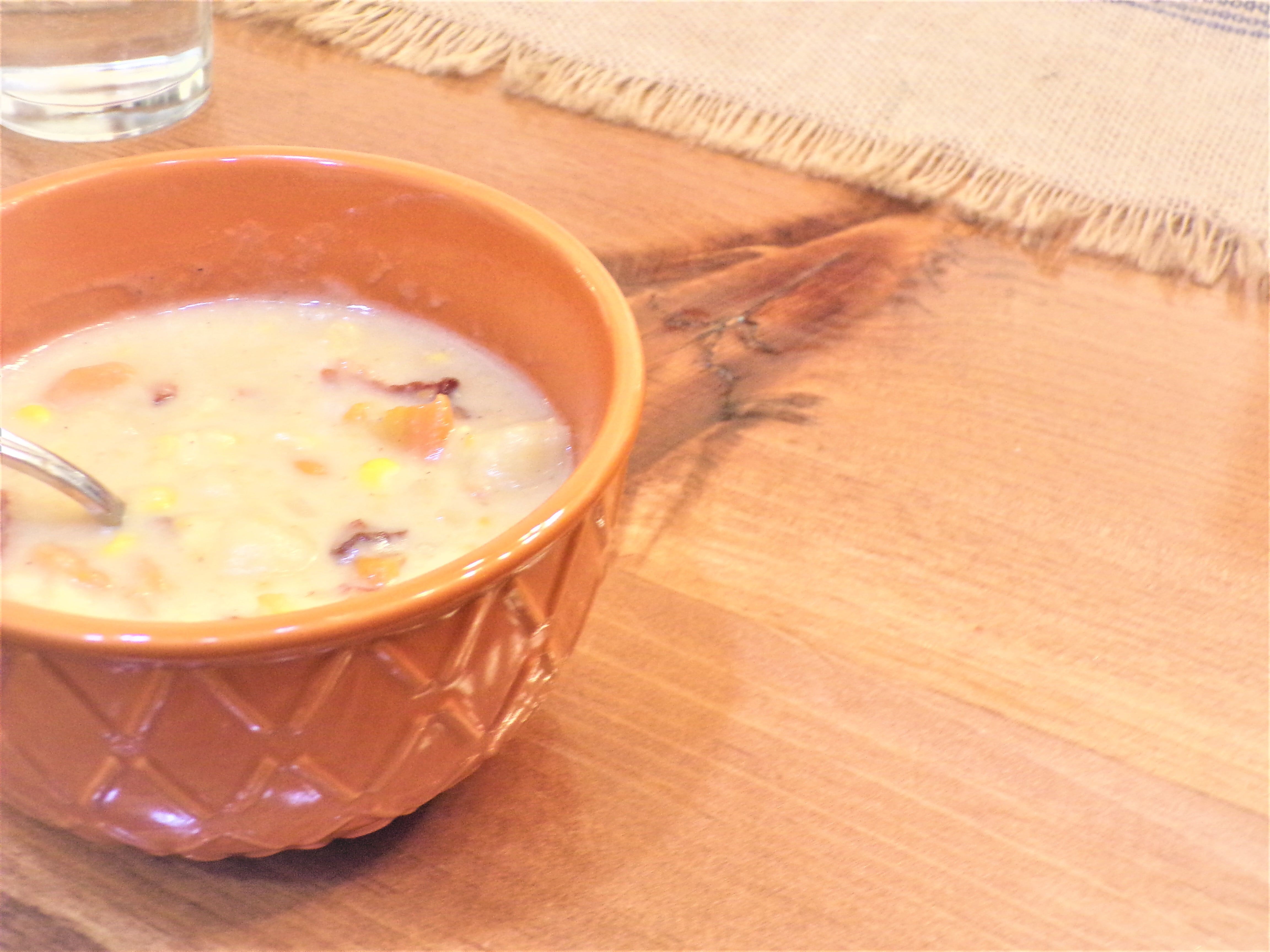 a bowl of creamy potato bacon corn chowder sits on a wooden table